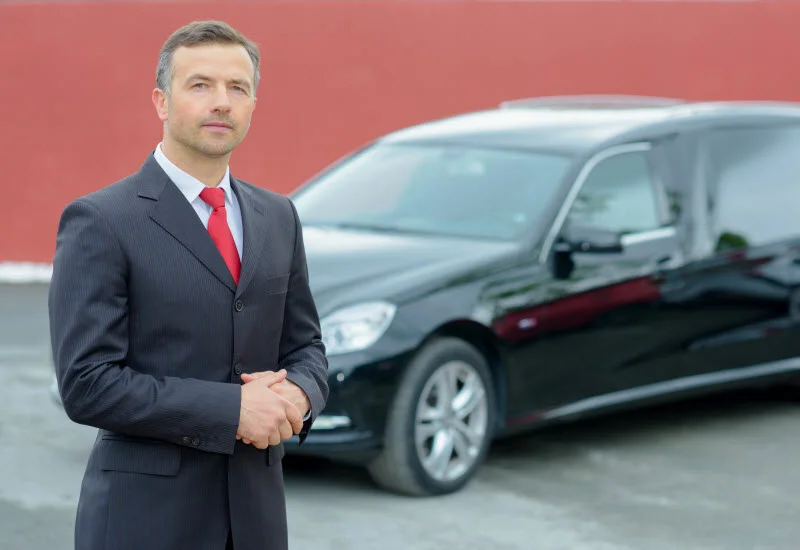 Man in suit in front of a funeral car