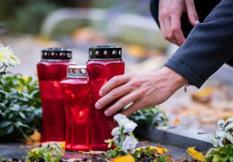 Man holding a red funeral candle placed on the tombstone