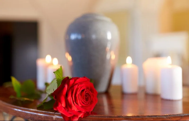 Urn with ash inside surrounded by candles and red rose